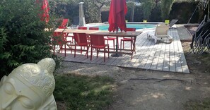 Une terrasse en bois avec une piscine, des chaises rouges et une statue blanche.