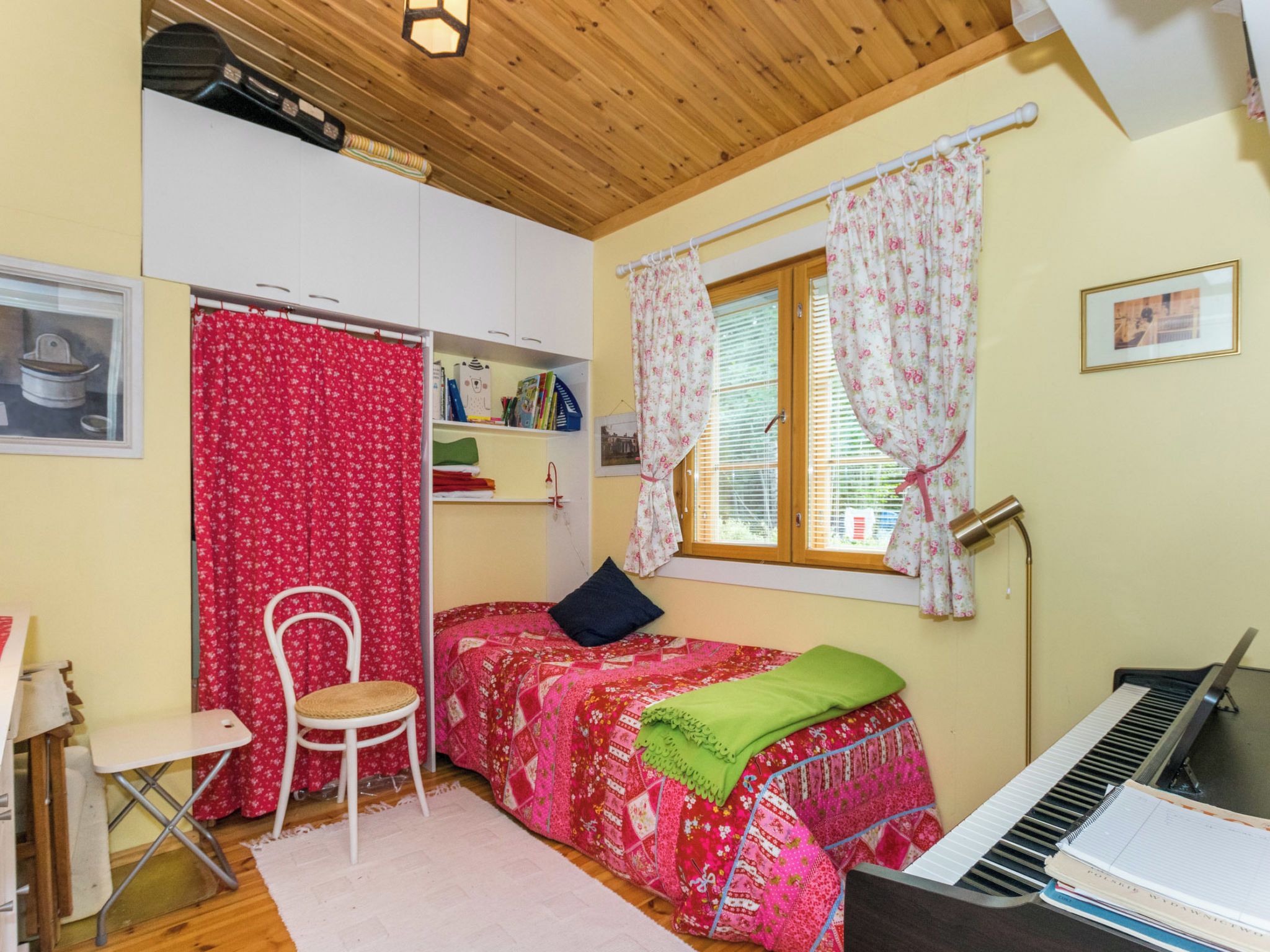 A bedroom with a bed, a chair, a piano, and a window with curtains.