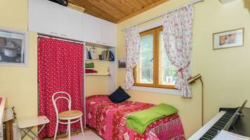 A bedroom with a bed, a chair, a piano, and a window with curtains.