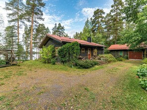 A cabin with a red roof, surrounded by a forest, a gravel path, and a wooden deck. - Metsä-iivari by Interhome (Lohja)
