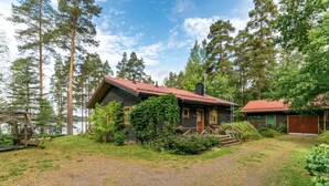A cabin with a red roof, surrounded by tall trees and a grassy area. - Metsä-iivari by Interhome (Lohja)