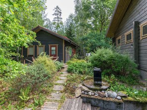 A wooden cabin with a stone pathway leading to the entrance, surrounded by dense greenery. - Metsä-iivari by Interhome (Lohja)
