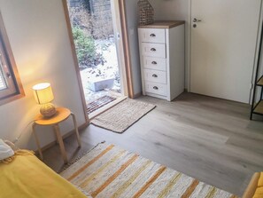 A room with a bed, a bedside lamp, a small table with a lamp, a white wardrobe, and a view of the outside. - Metsä-iivari by Interhome (Lohja)