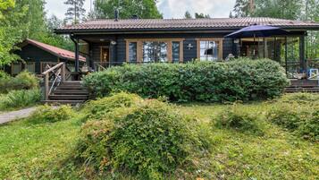 Een chalet met een veranda, een overdekte zithoek buiten en een verzorgde tuin.