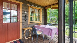 A wooden cabin with a covered porch, a table with a tablecloth, and a chair. - Metsä-iivari by Interhome (Lohja)