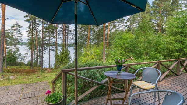 A wooden deck with a table and chairs, a potted plant, and a large umbrella. - Metsä-iivari by Interhome (Lohja)