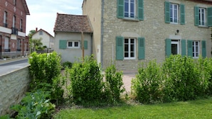 A stone building with green shutters, a paved driveway, and a grassy area with bushes. - Charming cottage in Saint-Bonnet-de-Rochefort with private garden (Saint-Bonnet-de-Rochefort)