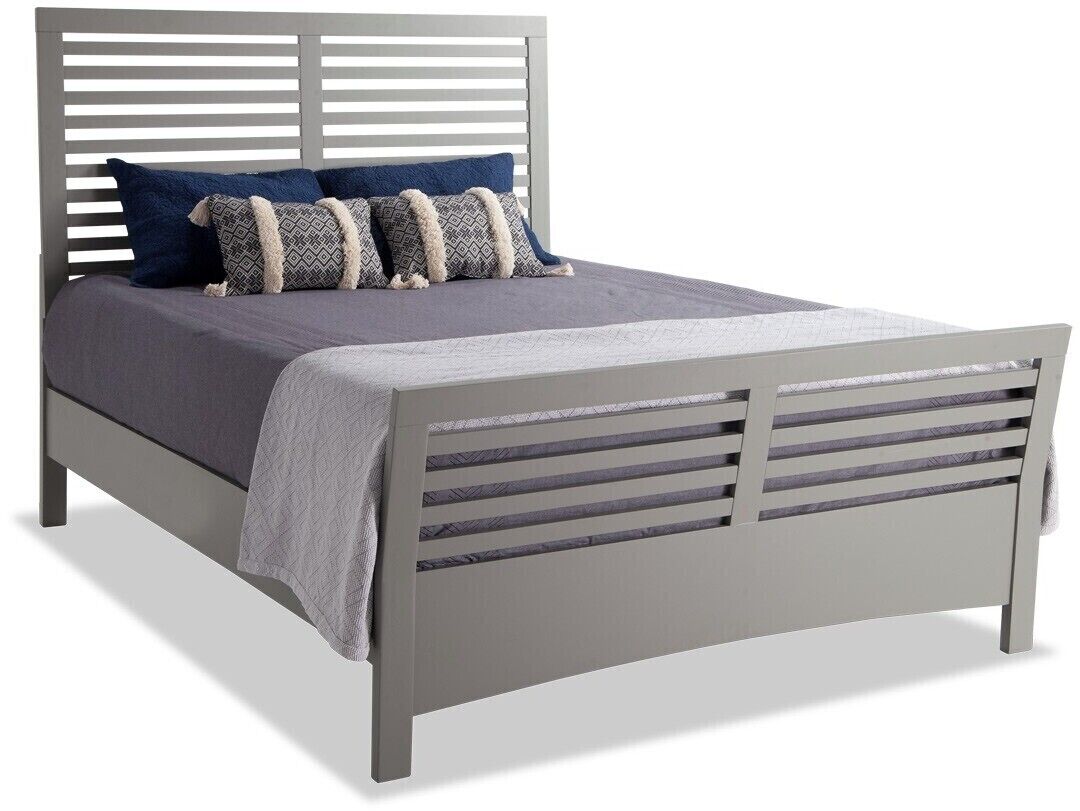 A bed with a headboard featuring horizontal slats, a grey mattress, and multiple pillows in various patterns.