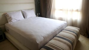 A neatly made bed with white linens, a bedside table, and a striped cushion. - Jnane Gueliz Residence 4053 (Marrakech)