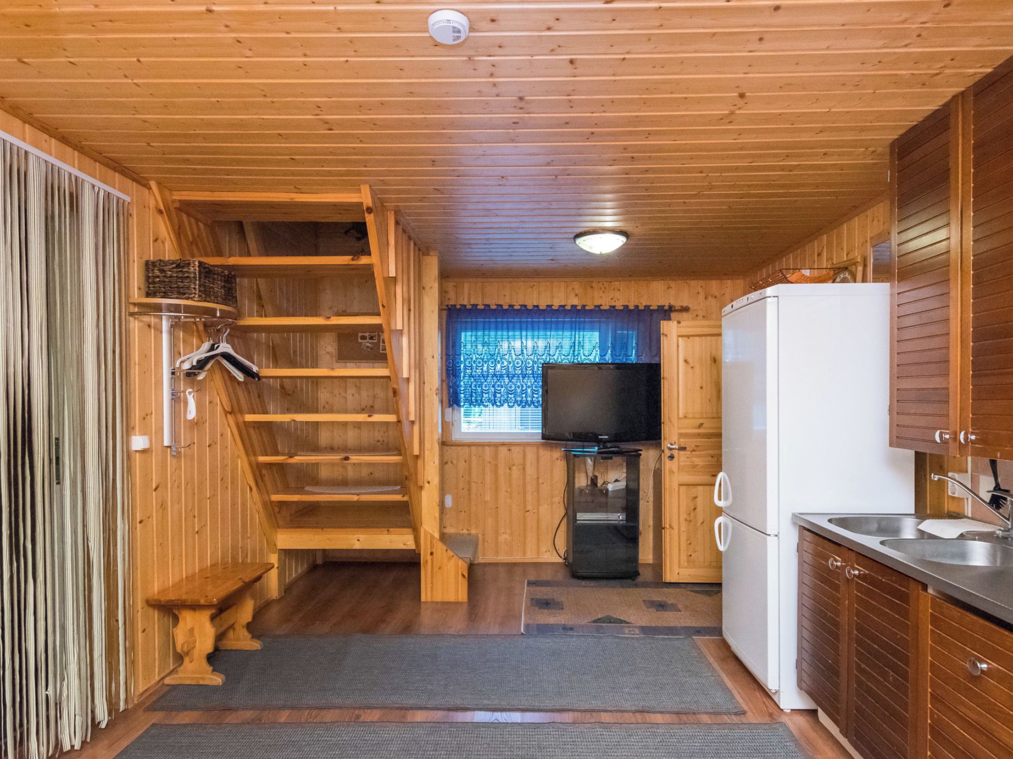 Een kleine keuken met houten wanden, een inbouwfornuis, een koelkast en een televisie.