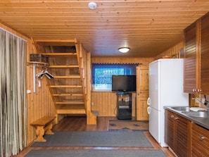A compact kitchen with wooden walls, a built-in stove, a refrigerator, and a television. - Vacation home Pöllö by Interhome (Kouvola)