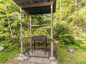 En rustik udendørs konstruktion med et metalbord og bænke, omgivet af frodig vegetation.