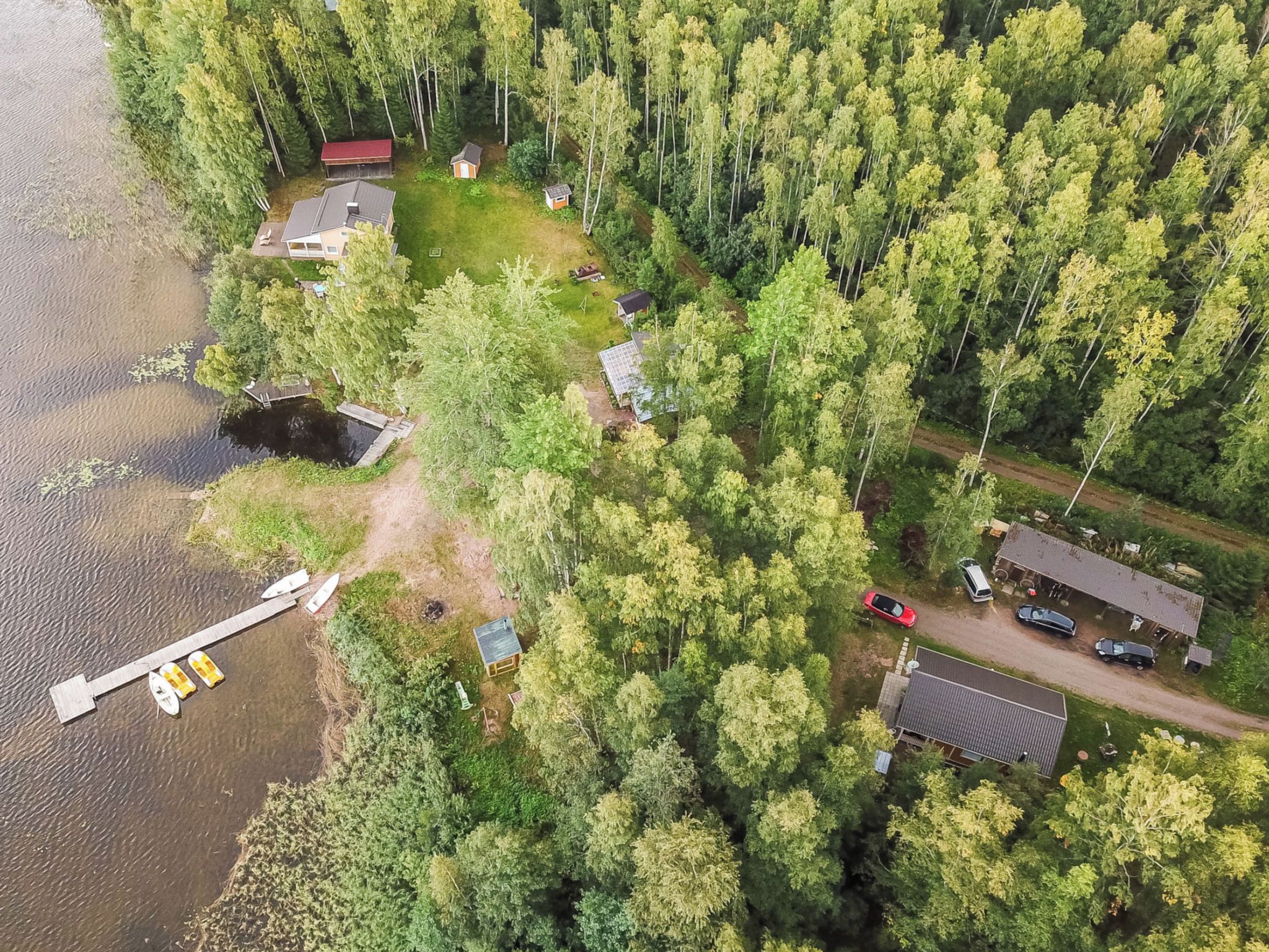 Vue aérienne d’une propriété au bord du lac, comprenant plusieurs chalets, un quai avec des bateaux et une forêt dense environnante.
