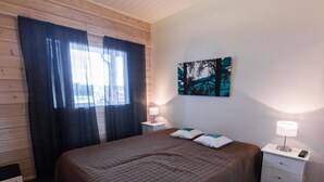 A bedroom with a large bed, a nightstand, a lamp, a painting on the wall, and a window with curtains.