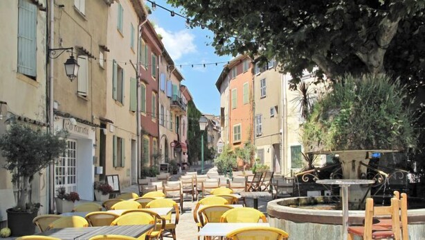Un cafè a l'aire lliure amb caires i taules grogues, envoltat d'edificis amb balcons i finestres.