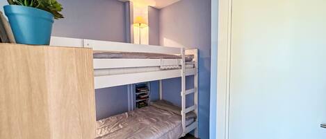 A bunk bed room with a potted plant, a bedside lamp, and a door.