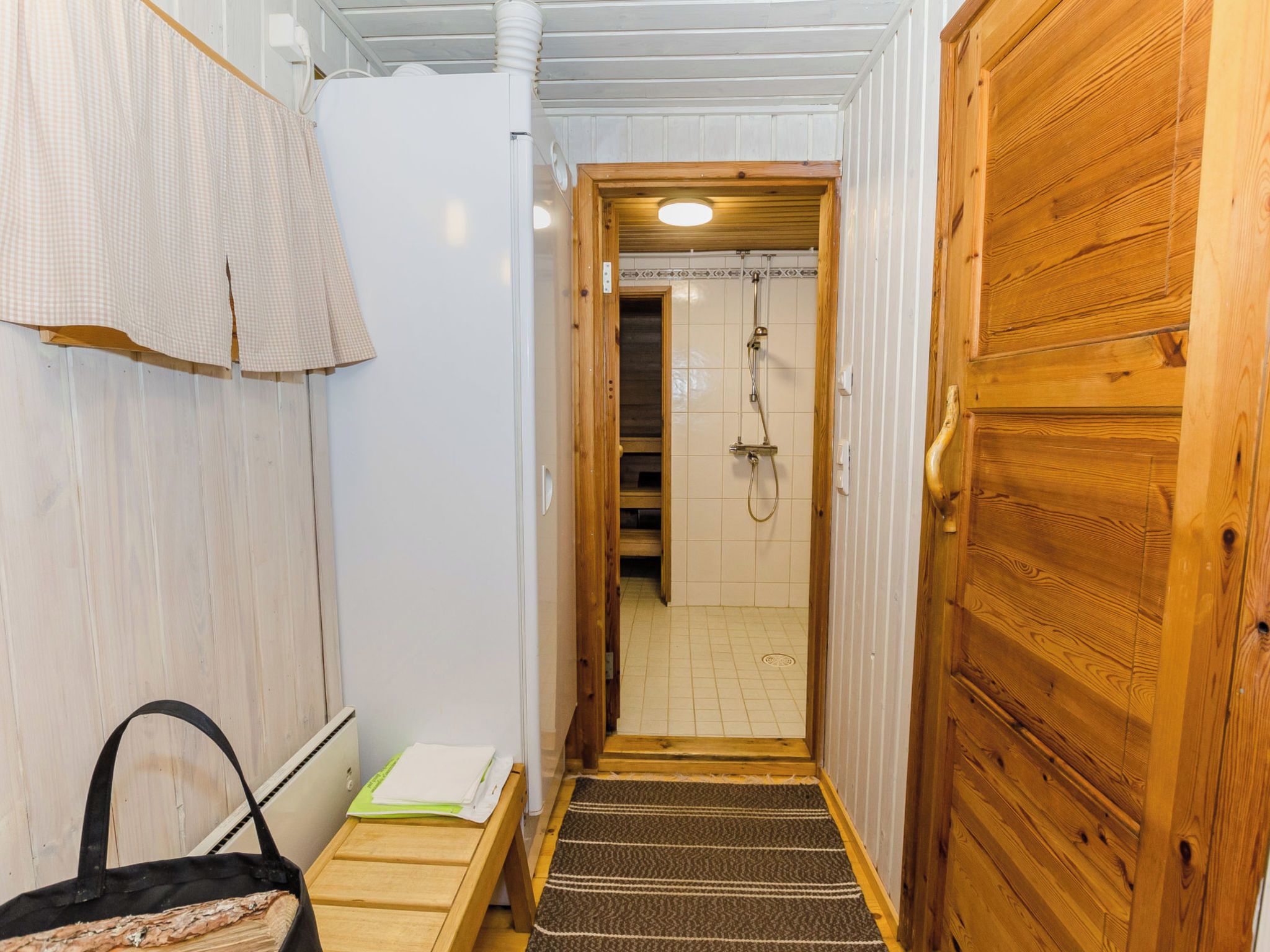 Corredor estreito que dá para um espaço com chuveiro, com uma porta de madeira à direita e um porta-toalhas à esquerda.