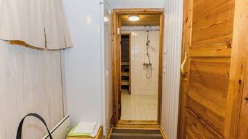 Corredor estreito que dá para um espaço com chuveiro, com uma porta de madeira à direita e um porta-toalhas à esquerda.