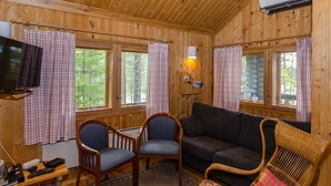 Interior de una cabaña de madera con sofá, dos sillones, una mesita y un televisor.