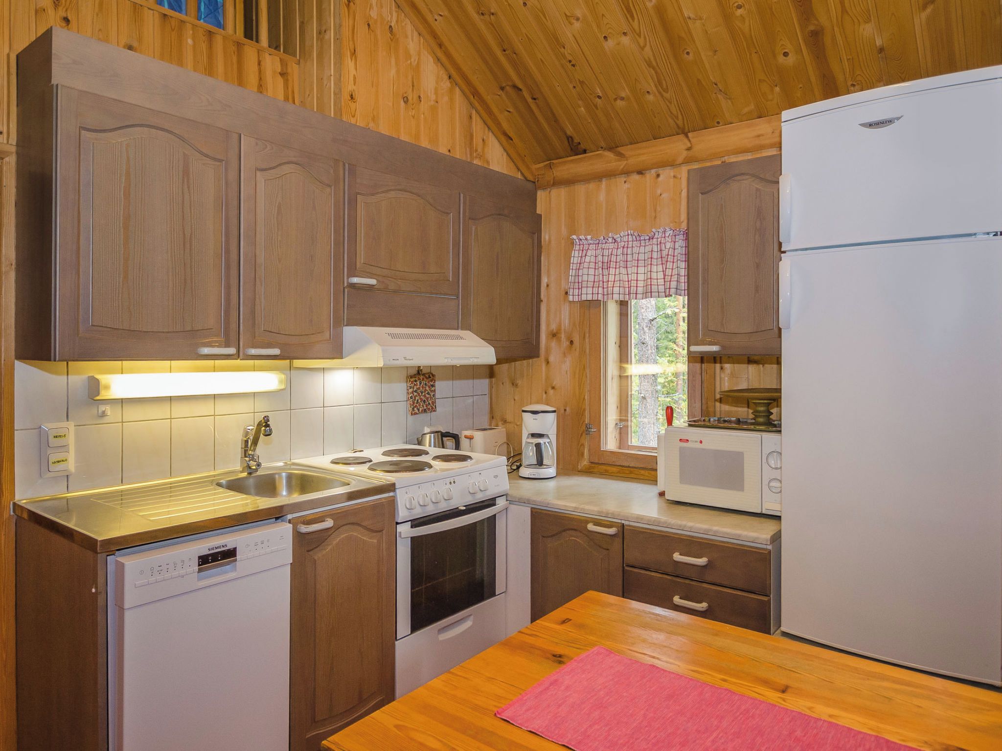 A compact kitchen with wooden cabinets, a Siemens dishwasher, a stove, a microwave, and a refrigerator.