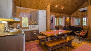 Una cocina acogedora de estilo cabaña con paredes y techo de madera. Hay una mesa con bancos, un sofá y un televisor montado en la pared.
