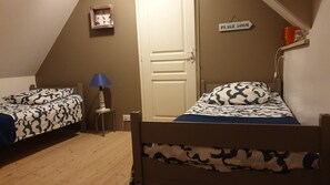 A bedroom with two single beds, a nightstand, a lamp, a door, and a sign indicating 'Plage 500M'.