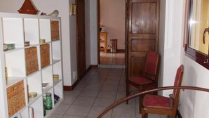 A hallway with a wooden chair, a white shelving unit with baskets, and a door leading to another room.