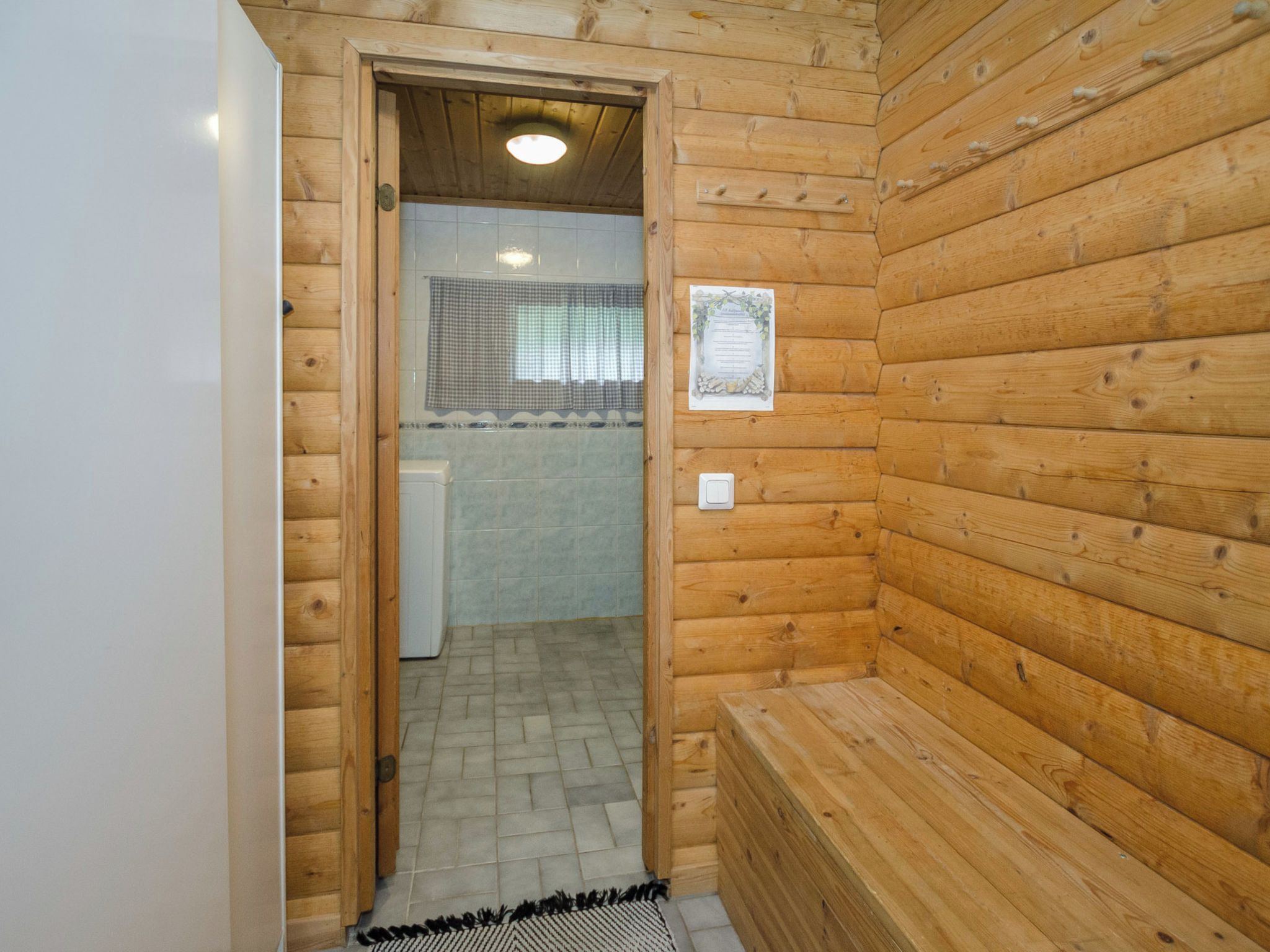 Een houten sauna met een bank, een betegelde vloer en een klein raam.