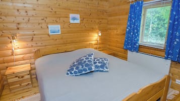 Una habitación de cabaña de madera con una cama, una mesita de noche y un ventanal con cortinas.