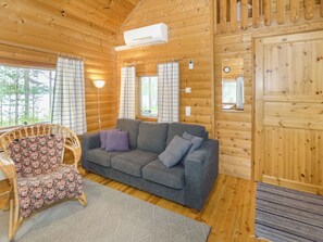 A cozy cabin interior with a grey sofa, floral-patterned chair, and wooden walls.