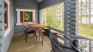 A log cabin with a wooden deck, a table with chairs, and a window overlooking a forest.
