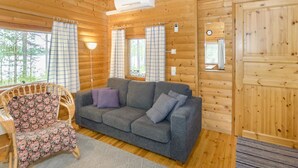 Interior acollidor d'una cabana amb un sofà gris, una cadira amb motius florals, parets de fusta i una finestra gran.