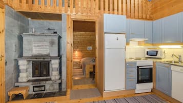 Una cuina compacta amb una llar de pedra, un refrigerador i un microones.