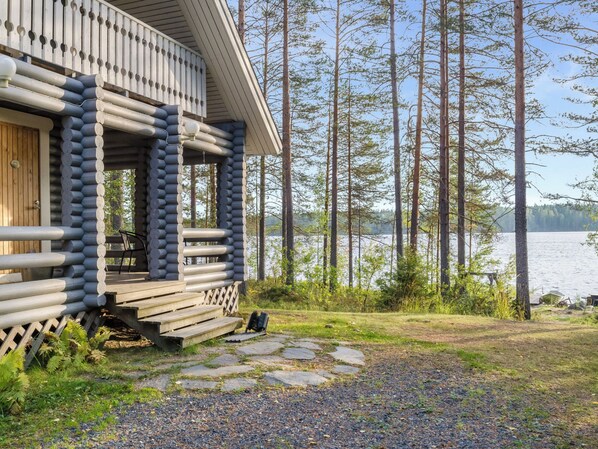 Hirsimökki, jossa on kuisti, kivipolku ja näkymä järvelle.