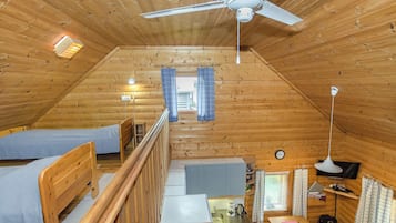 A cozy attic bedroom with a bunk bed, a desk, a small kitchenette, and a ceiling fan.