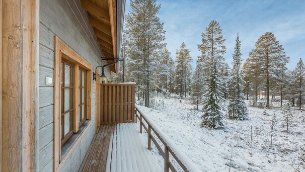 Una cabaña de madera con balcón que da a un bosque nevado.