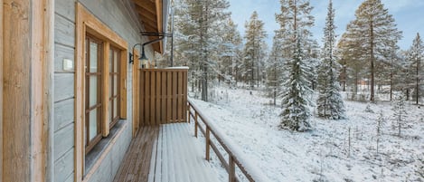 Une cabane en bois dotée d’un balcon donnant sur une forêt enneigée.