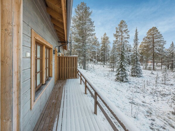 A wooden cabin with a balcony overlooking a snowy forest.