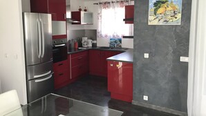 A compact kitchen with red cabinets, a stainless steel refrigerator, a coffee maker, and a painting on the wall. - Chalet in Provence with Pool, Parking, Wifi, Near Avignon, Luberon ... (Sorgues)
