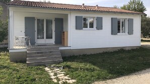 A single-story house with a tiled roof, a front porch with a table and chairs, and a small set of steps leading to the entrance. - Chalet in Provence with Pool, Parking, Wifi, Near Avignon, Luberon ... (Sorgues)