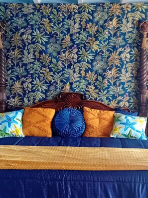 Cama com colcha azul e dourada, cabeceira floral e almofadas decorativas.