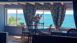 Una zona de menjador amb taula i cadires, un vas amb flors, i vista a l'oceà a través de grans finestres.