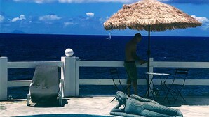 Zona de piscina amb una estàtua, gandules i un parasol de palla.
