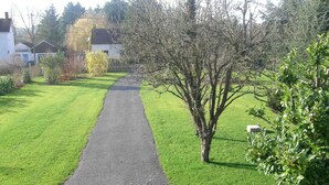 Un chemin pavé aménagé dans un espace verdoyant bien entretenu, agrémenté d’arbres et d’arbustes.