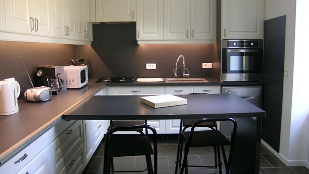 Une cuisine moderne avec des meubles blancs, un îlot central, des tabourets de bar noirs, un four à micro-ondes, une cuisinière et un four.
