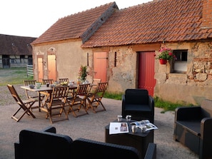 Un espace extérieur aménagé pour les repas, avec une table et des chaises, un canapé en osier et une porte rouge.