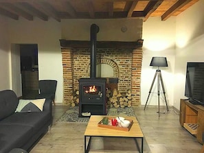 Un salon avec une cheminée en pierre, un canapé, une table basse avec quelques objets, une lampe et un téléviseur.