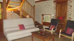 Un salón acogedor con una escalera de madera, un sofá blanco, dos sillones y una mesa de centro con un ovillo de hilo.