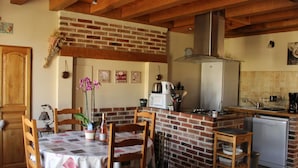 Una cocina acogedora con pared de ladrillo, vigas de madera en el techo, una mesa de comedor con sillas y una isla de cocina con estufa y microondas.