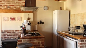 Una cocina con pared de ladrillo, estufa, refrigerador y un reloj en la pared.